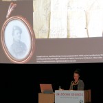 Speaker at a conference podiem, with slide showing a mstory about a matchbox from WW1