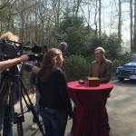 Camera crew interview contributor in front of vintage cars